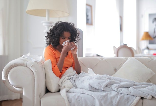 A woman laying sick on the couch, sneezing